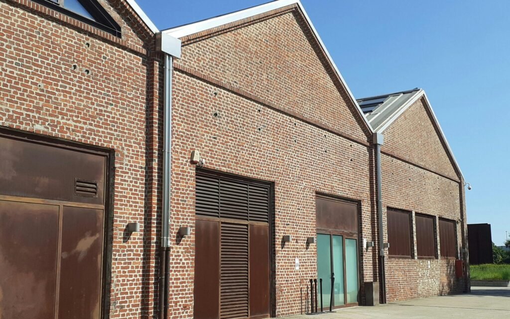 Industrial red brick warehouses with wooden doors in daylight, clear sky above.